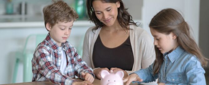 A mom helps her kids count money in front of a piggy bank.