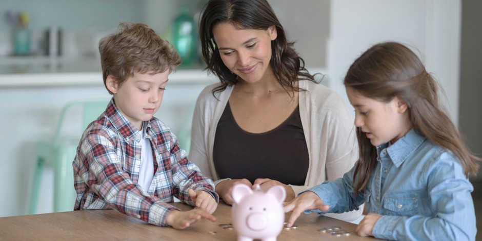 A mom helps her kids count money in front of a piggy bank.