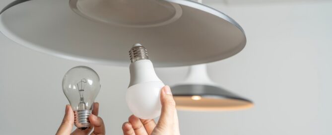 A person replaces an incandescent light bulb with a more energy-efficient bulb.