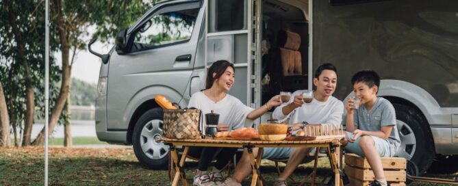 A family has a picnic next to their travel camper.