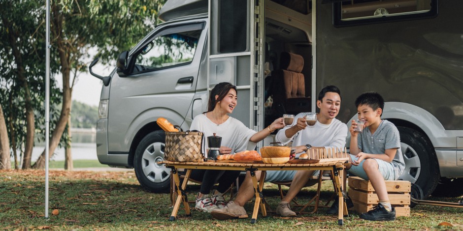 A family has a picnic next to their travel camper.