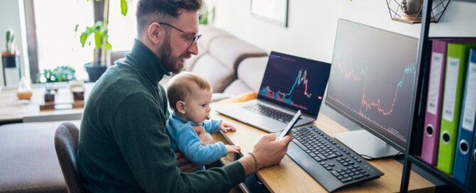 A man with a baby on his lap checks his investments.