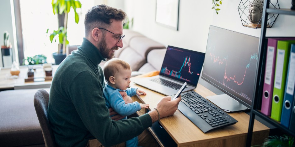 A man with a baby on his lap checks his investments.